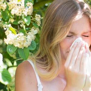 Frau, die sich im Grünen vor einer Obstblüte die Nase putzt wegen allergischer Reaktion