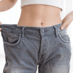 Abnehmen mit Hypnose? Und warum ist Abnehmen so schwer? Frau mit freiem Bauch in einer Jeans, die sehr viel abgenommen hat und die Hose jetzt viel zu weit ist.